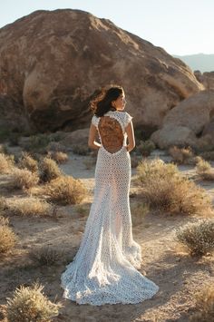 a woman standing in the desert with her back to the camera, wearing a white crocheted dress