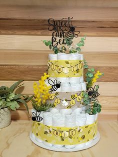 a three tiered cake with bees and flowers on it's sides, sitting on a wooden table