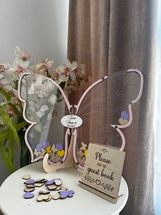 a white table topped with a vase filled with flowers and butterfly magnets next to a sign