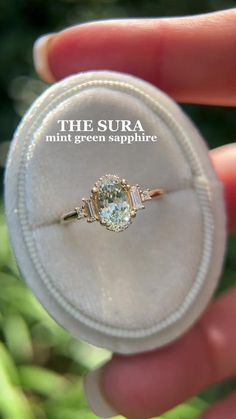 a person holding a ring in their hand with the words, the sura mini green sapphire