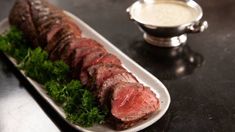 some meat is on a white plate and garnished with parsley next to a silver bowl