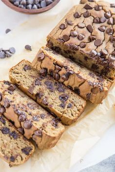 sliced loaf of chocolate chip banana bread sitting on top of parchment paper next to a bowl of chocolate chips