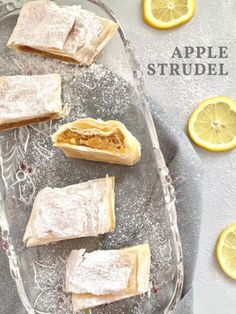 an apple strudel is on a glass platter with lemon slices around it