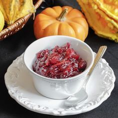 a white bowl filled with cranberry sauce on top of a plate next to pumpkins