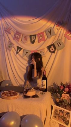 a woman sitting in front of a table with pizza and wine on it, surrounded by balloons