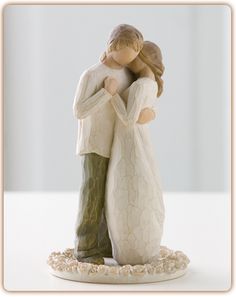 a figurine of a couple hugging each other on a white surface with one holding the other's head