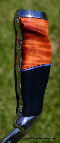 an orange and blue vase sitting on top of a metal handlebar with grass in the background