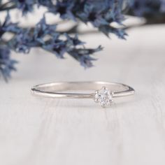 a diamond ring sitting on top of a wooden table next to blue flowers and branches