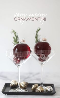 two wine glasses with ornaments in them sitting on a tray that says very merry ornamentii