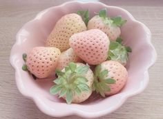 a pink bowl filled with strawberries on top of a wooden table