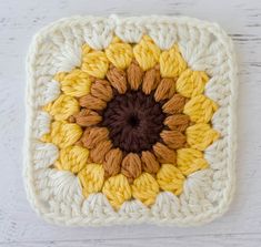 a crocheted square with an orange and yellow flower in the center on a white wooden surface