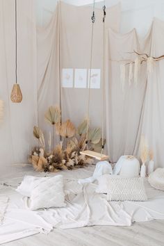 the bed is covered with white sheets and pillows, along with dried plants in vases