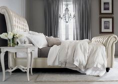 a white bed sitting under a window next to a table with flowers on top of it