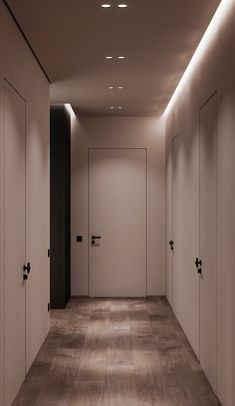 an empty hallway with white walls and wooden flooring is lit by recessed lights