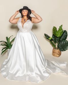 a woman in a white dress and black hat posing for a photo with her hands on her head