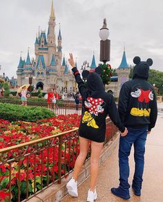 a man and woman in mickey mouse hoodies standing next to each other near flowers