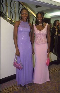 two women standing next to each other in long dresses and holding purses on their laps