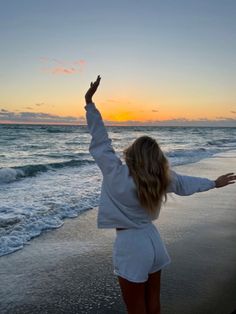 a woman standing on the beach with her arms in the air and hands up to the sky