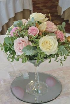 a glass vase filled with pink and white flowers on top of a table covered in tables cloths