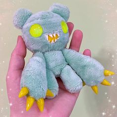 a hand holding a blue stuffed animal with yellow spikes on it's claws and eyes