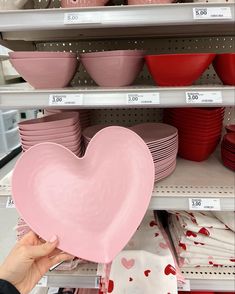 a person holding a heart shaped plate in front of plates on the shelves at a store