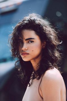 a close up of a person wearing a dress and looking off to the side with a car in the background