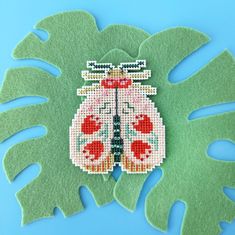 a cross stitched insect sitting on top of a green leaf