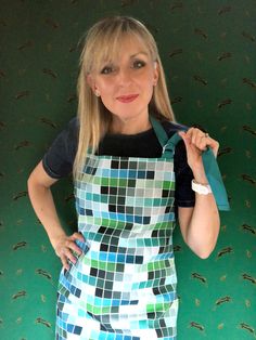 a woman in an apron is holding up a green bag and posing for the camera