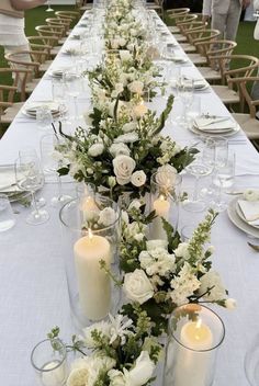 a long table with white flowers and candles on it is set for an outdoor dinner