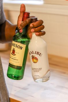 a person holding two bottles of alcohol in one hand and an empty bottle in the other