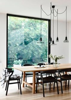 a dining room table and chairs in front of a large window with trees outside it