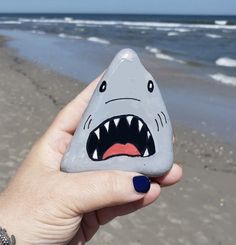 a hand holding a rock with a shark's mouth painted on it at the beach