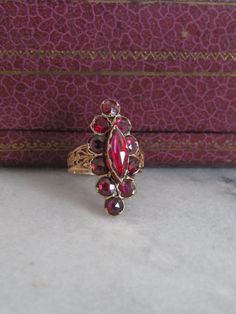 This lovely marquise ring is crafted from high carat gold and foil backed garnets. Known as "Perpignan garnets" or "Catalan garnets" these are regional jewels crafted near Perpignan, in the Pyrenes foothills close to the the Spanish border. A popular style from the late 18th to early 19th centuries, these jewels were often passed down from mother to daughter. The garnets are rose cuts, which are artfully foiled and set in gold to achieve a distinctive deep-pink hue which reflects light beautiful Gold Marquise Ruby Ring, Vintage Red Marquise-cut Jewelry, Vintage Red Marquise Cut Jewelry, Red Garnet Marquise Ring, Marquise Garnet Red Rings, Garnet Gemstone Ring In Marquise Cut, Red Marquise Rose Cut Diamond Rings, Marquise Garnet Ring In Red, Red Marquise Rings With Rose Cut Diamonds