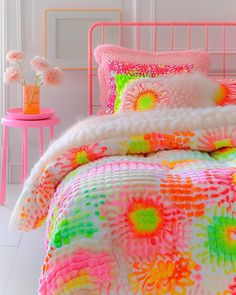 a bed with pink, green, yellow and orange comforter on top of it