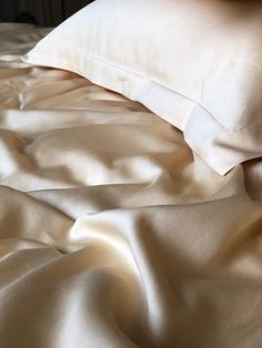 an unmade bed with white sheets and pillows