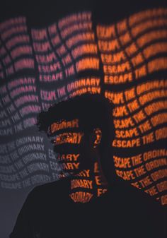 a man standing in front of a wall with words projected on it's face