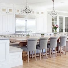 a large kitchen with white cabinets and an island in the center is surrounded by gray chairs