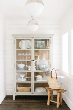 a white china cabinet with glass doors and dishes on it's shelves in a dining room