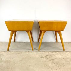 two wooden stools sitting next to each other on cement floored area with white wall in background