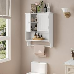 a white toilet sitting next to a window in a bathroom under a shelf above it