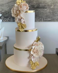 a three tiered wedding cake with gold leaf and flowers on the top, sitting on a table