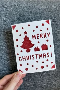 someone holding up a christmas card with the words merry christmas written in red on it