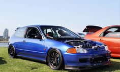 two cars parked next to each other in the grass with their hoods open on