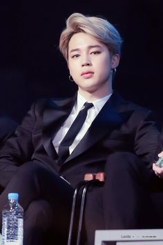 a man in a suit sitting on a chair next to a water bottle and microphone