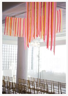 a room filled with lots of chairs covered in pink, yellow and orange streamers