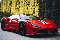 a red sports car is parked in front of some green bushes and tall trees on the street