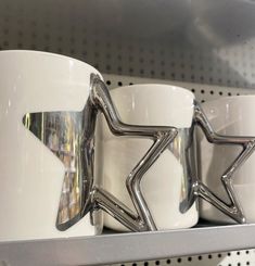 three white mugs with silver stars on them sitting on a shelf in a store