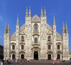 people are walking around in front of a large building with many towers and spires