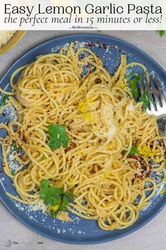 a blue plate topped with pasta and parsley next to a fork on top of a table