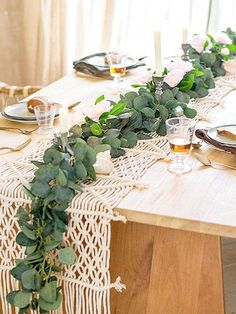 the table is set with place settings and greenery on it, along with candles